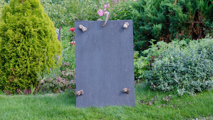 Slate sign with rope detail set against a garden backdrop. Copy space.