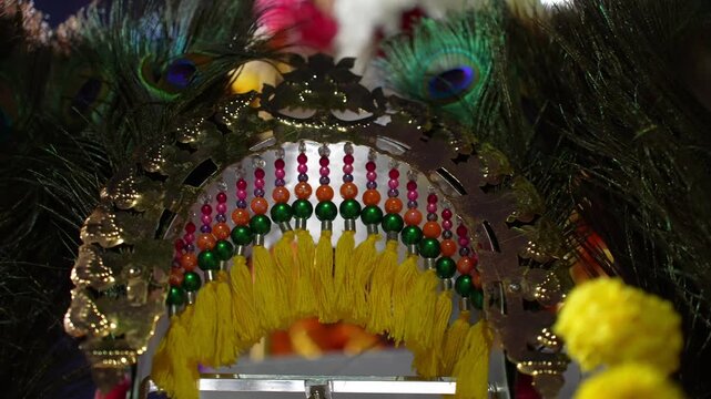 A gold and green peacock decoration with yellow and green feathers. The peacock feather is hanging from a tree