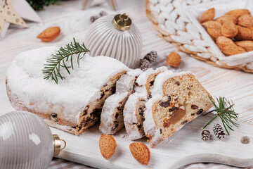 Christmas stollen bread garnished with powdered sugar, surrounded by festive decorations, almonds, and ornaments on a cozy holiday table.