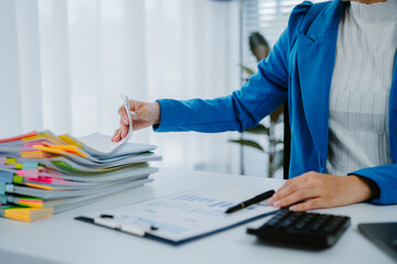 Asian businesswoman sitting using laptop, searching for data, holding graph documents