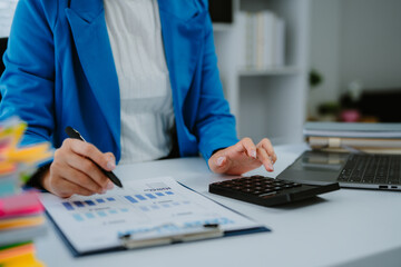 Young Asian businesswoman smiling and working on laptop computer, standing at desk in modern office, enjoying work, browsing internet, searching information, online meeting, video conference