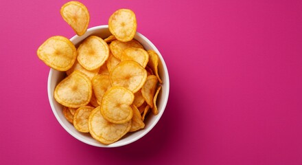 鮮やかなピンク背景に映える、カリカリとしたバナナチップス。白いボウルに山盛りに盛られ、軽快に飛び跳ねる様子が食欲をそそる一枚