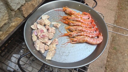 Traditional spanish paella with fresh seafood and meat ingredients in outdoor cooking setting. Typical cuisine of Spain. Valencian cuisine. Stage of cooking paella. Ingredients for paella