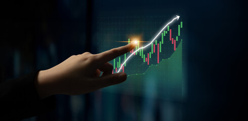 A close-up of a hand interacting with a stock market graph displaying an upward trend. The image...