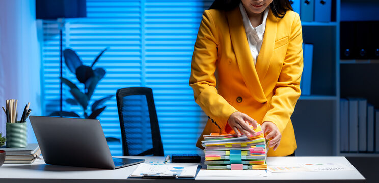 Organized Workflow: A sharp woman, meticulously sorting through a stack of files on her desk, symbolizing precision and professionalism in a dynamic office setting.