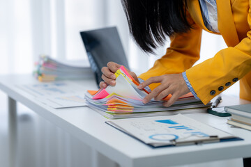 Overwhelmed by Paperwork: A businesswoman grapples with a towering stack of documents, her desk...