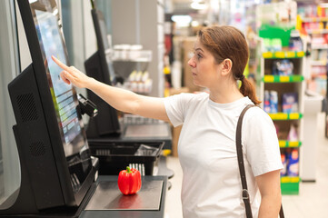 A woman buys bell peppers at a self-checkout. 