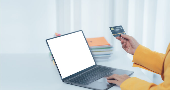 Digital Payment: A person's hand firmly grasps a credit card, hovering over a laptop's keyboard in a modern setting.