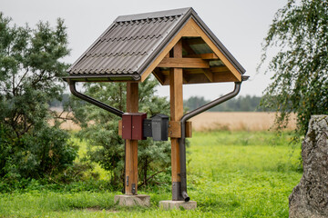 Rural wooden structure with sloped roof sheltering mailboxes in countryside setting, functional and decorative utility construction for village post delivery in scenic natural environment