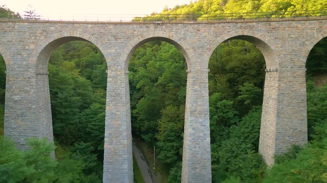 Experience the majestic Zampach railway bridge, the tallest stone bridge in Czechia, surrounded by lush greenery and scenic vistas during a captivating golden hour.