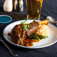 Rich Curried Lamb Shank with Rice and Green Beans on a White Plate closeup side view of Asian fusion food