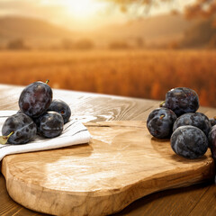 Seasonal fruit of plums on wooden table. Empty copy space  for product placement or text. Golden fall sky with warm and earthy tones.