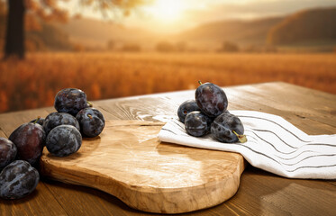 Seasonal fruit of plums on wooden table. Empty copy space  for product placement or text. Golden fall sky with warm and earthy tones.
