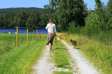 Woman walking with dog at country road one summer day. Bergslagen, Sweden.