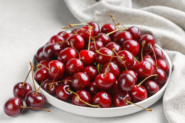 Close up of white plate filled with ripe red sweet cherry placed on gray linen napkin on light background. Delicious food, juicy summer fruit and healthy eating.