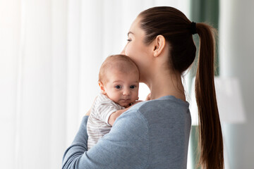 Maternal Mental Health Problems. Young Woman Holding Cute Little Newborn Baby Standing Near Window At Home, Upset Pensive Millennial Mother Suffering From Postpartum Depression, Copy Space