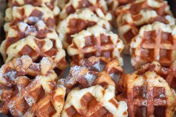 Golden brown waffles with powdered sugar stacked on a buffet tray.