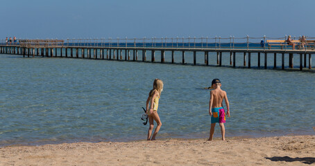 Hurghada, Governorate - Red Sea, Egypt - 19.11.2024. A little boy and a girl walking along the coastline of the Red Sea.