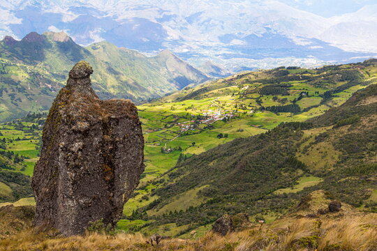 Huge rock, panoramic view of a mountain range, valley and village from the top of the Bolarrumi Rock Complex located on highlands of the Huasipamba community, Santa Isabel, Azuay, Ecuadorian Andes