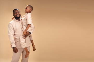 In soft studio light, a father and son in matching beige share a quiet, heartfelt smile. The...