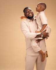 Framed in soft beige, a father cradles his son, their smiles reflecting roots, resilience, and a...
