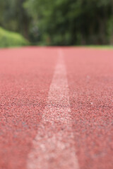 Red running track with white line. Running track in the park with selective focus. Running track surface close-up. Marked white line on the sports field. Background