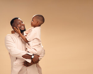 An African father and son gaze warmly at each other in matching beige outfits. Soft studio light...