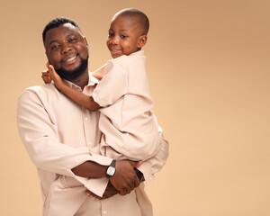 A joyful African father embraces his smiling son, both dressed in matching beige. Set against a...