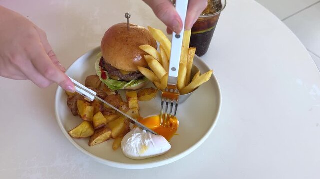 cut an egg on a plate with a knife and fork Girl Consuming Fast Food Fries And A Meat Burger In A Cafe. High quality 4k footage