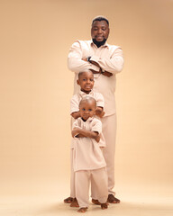 A father and his sons stand with folded arms in matching beige, bathed in warm light. Their steady spirits and calm strength reflect leadership, love, and the enduring power of family unity.
