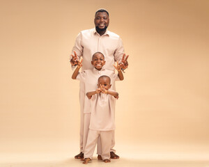 A father and his two sons flash peace signs, beaming with joy in matching beige. Soft studio light...