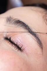 Obraz premium An unrecognizable woman waxing a client's eyebrow with white thread inside a beauty salon in Neiva, Huila, Colombia. Handmade and waxing concept