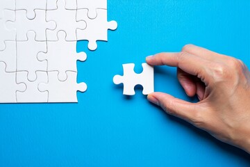 Puzzle completion concept with hand placing piece on blue background for problem solving