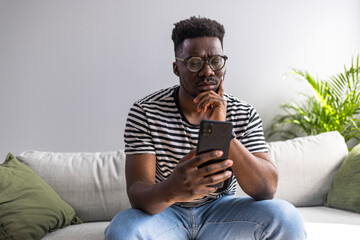 Young Man Using Smartphone While Sitting Thoughtfully in a Modern Living Room