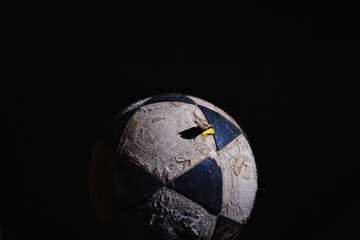 Damaged yellow, black, and white soccer ball against a black background