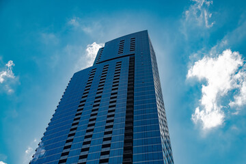 Naklejka premium Luxury real estate skyscraper with glass facade. Elegant residential architecture set against bright clouds and sky.