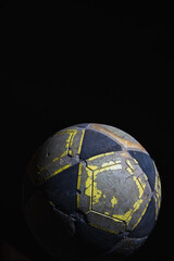 Damaged yellow, black, and white soccer ball against a black background