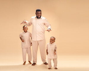 Smiling Black father barefoot with two young sons in matching beige outfits, joyful family portrait...