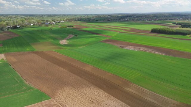 Aerial panoramic shot of expansive patchwork fields in spring, displaying colorful farmland and rural countryside.