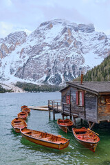 March 2025: view of Braies Lake in winter, with a frozen surface marked by trails, surrounded by snow covered cliffs, rugged rocks, and evergreen trees.a