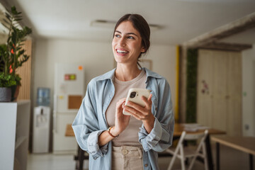 Happy businesswoman using mobile phone in office break room
