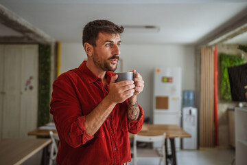 Creative man drinking coffee and thinking in modern office kitchen