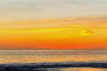 Golden sunset over a calm ocean with soft waves and vivid orange sky. Peaceful tropical seascape.