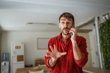 Surprised man receiving bad news on mobile phone at home