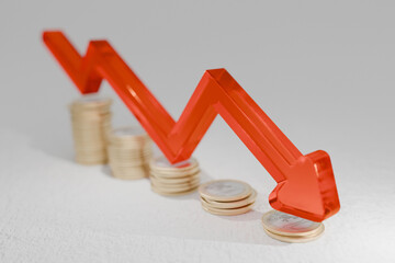 Decreasing stacks of coins with a red downward arrow illustrate economic decline, inflation impact,...