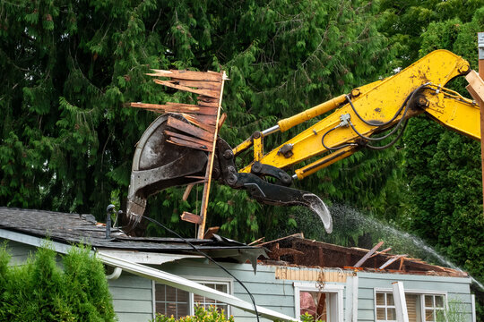 Demolition of old wood frame house for redevelopment of residential property using a large excavator machine with jawbone bucket

