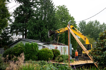Workman with hose spraying water on demolition of old wood frame house for redevelopment of...