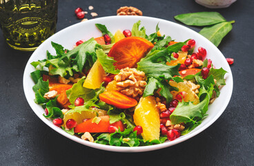 Delicious vegan salad with fresh persimmon, pomegranate seeds, walnuts, orange slices and lettuce