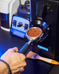 Close-up of a barista grinding fresh coffee into a portafilter using a professional espresso grinder, with bar tools in the background.