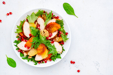 Yummy persimmon salad with grilled chicken, pomegranate, walnuts, oranges and lettuce, top view